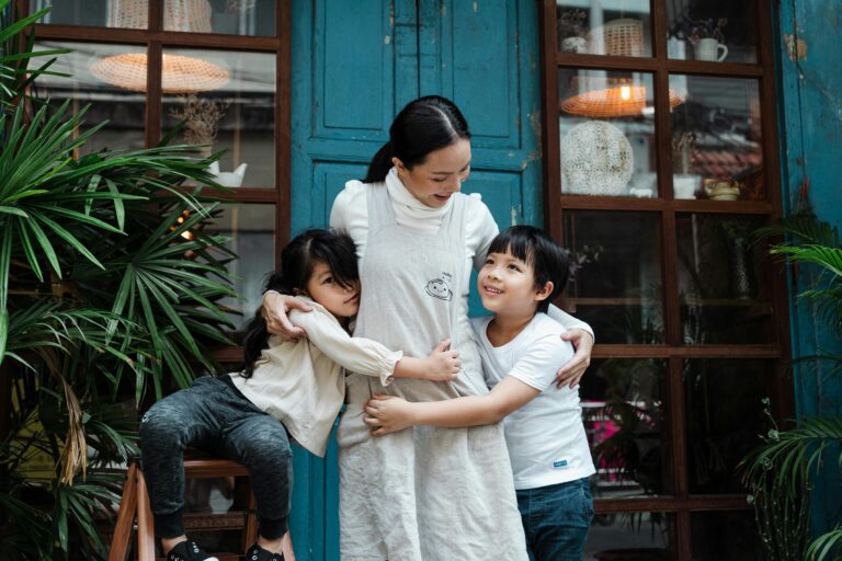 A mother embraces her two children in a loving, joyful moment outside a rustic blue door.